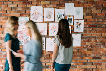 Naklejka premium art studio workspace. painter artwork. girl looking at watercolor drawings of flowers and animals on the wall