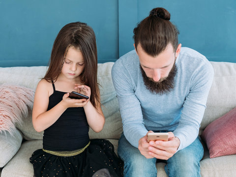 Modern Family Problems. Internet Addiction. Mobile Devices Overusage. Dad And Kid Sitting On Sofa And Staring At Their Phones. Technology Invasion Into Child Upbringing.