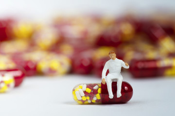 Miniature people with medical drug capsule on white background