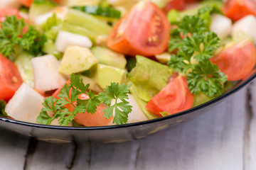 Delicious salad of vegetables, turnips, cucumber, tomato, avocado and parsley on a white background