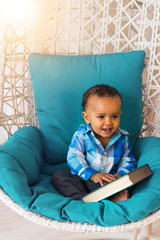 Portrait of African American baby boy holding book on chair.