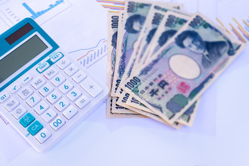 Calculator with blurred Japanese currency yen bank notes and coin on finance chart and graph background, finance planning concept