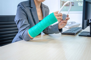 woman with broken hand and green cast  working on computer and holding headphone