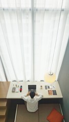 Working on the laptop by the white-curtained window in a luxury, business loft in Singapore. 