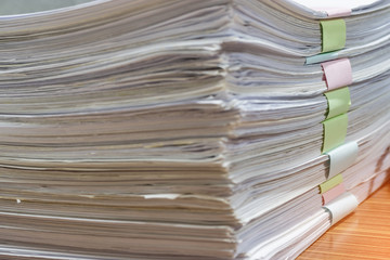 Close up pile of unfinished homework assignment stacked in archive with colorful papers on teacher's table waiting to be managed and inspected. Stack of  paperworks. Education and business concept.