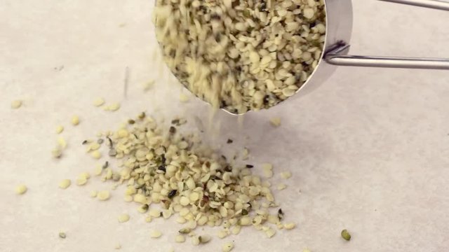 Hemp seed hearts poured from a metal measuring scoop (1/4 cup) on a light ceramic tile