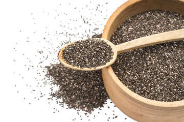 Close up of chia seeds in wooden spoon on top of a wooden bowl with some spread on the blurred white background seen obliquely from above