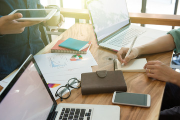 Naklejka premium business team analyzing marketing strategy with smart phone, tablet, notebook, and laptop on wooden desk with,Freelance work at home office.Team work and helping hand