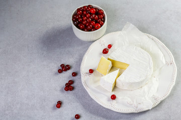 Cheese Camembert or brie and cranberries, with a cut piece, on paper Isolated on kitchen table...