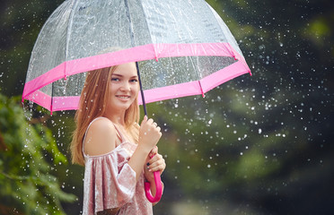 A teenage girl hid from the rain under an umbrella while walking through the park. She laughs and...