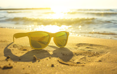 Yellow sunglasses on yellow sand beach with blue sea and sky background summer