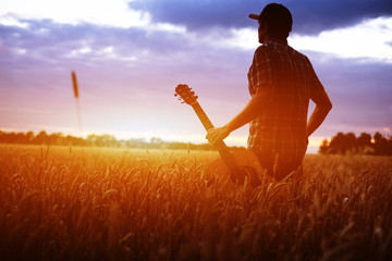 Musician with guitar at sunset field.