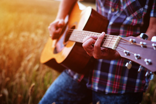 Musician playing guitar at sunset field.