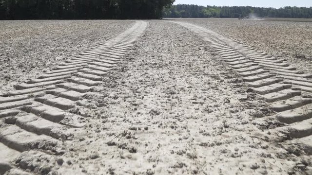 Large tire tracks in field with tractor in the background