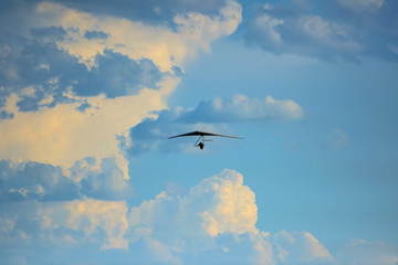 Silhouette of hang glider against blue sky with thunderclouds. Copy space.