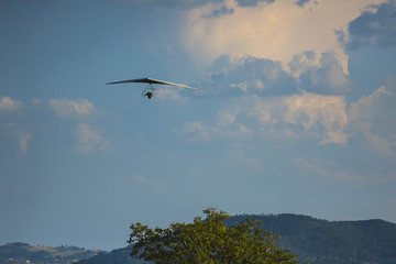 Silhouette of hang glider against blue sky with thunderclouds. Copy space.