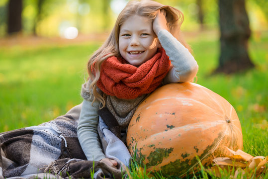 Little girl with large pumpkin outdoor in autumn park
