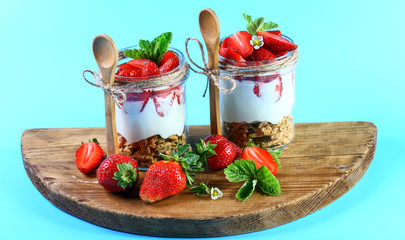Healthy layered dessert with cream, muesli on a wooden board, isolated on a blue background. top view image with copy space