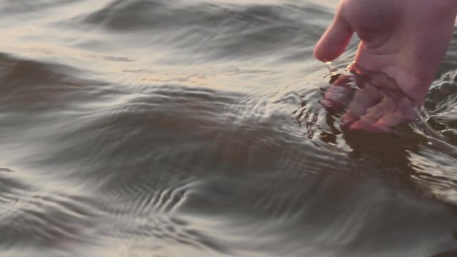 Slow motion closeup young female hand touches water waves at sunset