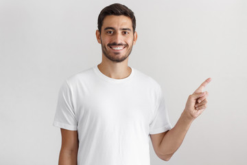 Young man in white t-shirt pointing right with his finger isolated on gray background