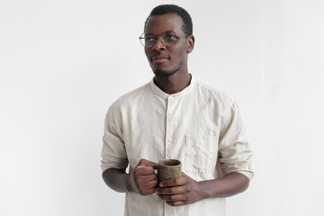 Young african american man isolated on gray background standing in casual shirt with ceramic mug in...