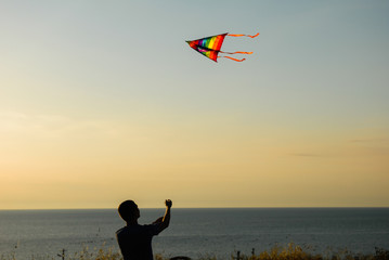silhouette of young healthy man leading flying colorful kite in autumn sunset
