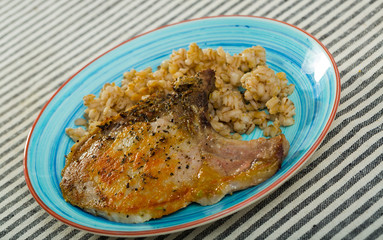 Barley groats with frying pork loin at plate on table