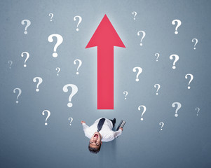 Young contemplating businessman stands in front of a big red arrow and white question marks