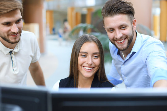 Group of young people in casual wear sitting at the office desk and discussing something while looking at PC together.