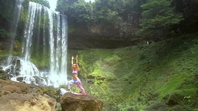 girl raises hands to change yoga pose on rock