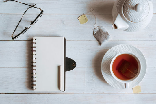 Cup of tea with notebook on white wooden table, Top view