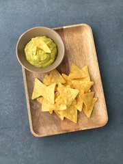 Chips nachos on a wooden plate. Next to a bowl with Mexican green salsa sauce. Gray background. View from above. Close-up.  Vertical orientation of the frame.