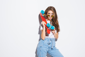 Portrait of a happy cheerful woman in sunglasses posing with skateboard while standing isolated over white background