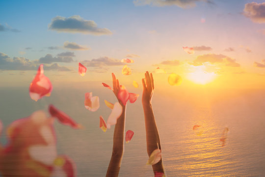 Celebration, happiness, joy concept.  Hand throwing rose pedals in the air against a beautiful sunset. Double exposure.