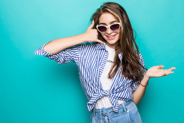 Portrait of attractive happy girl with glasses gesturing with fingers call me isolated on blue background