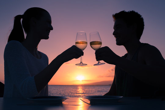 Happy couple enjoying wine by the sea at sunset.
