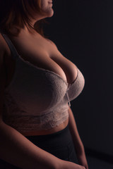 Naklejka premium Young beautiful busty curvy plus size model with big breast in white bra, xxl woman. Black background.