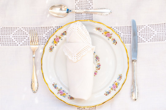 Flatlay of a dessert set: porcelain plates with silver cutery and lace napkins.