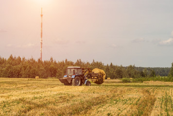 Farmer on a tractor picks haystack and loads bale of hay into the trailer, agriculture