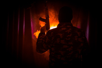 Silhouette of man with assault rifle ready to attack on dark toned foggy background or dangerous...