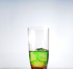 Transparent glass Cup with green drink and ice cubes.