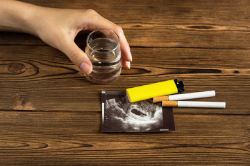 A woman's hand holds a glass of alcohol, next to it is a photograph of the uzi pregnancy and cigarettes, pregnancy and smoking, cigarette