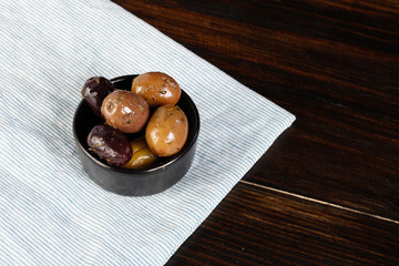 Black and green olives in wooden plate on wooden background. Salted olives. International cuisine. Harvesting.