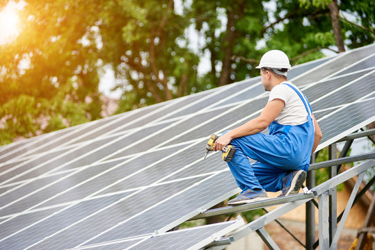 Construction worker with screwdriver connecting photo voltaic panels on solar system shiny surface background. Alternative energy, ecology protection and cheap electricity production concept.