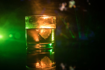 selective focus pure whisky with ice cube inside whisky glass on dark foggy background alcohol drink concept.