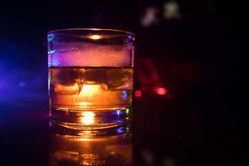 selective focus pure whisky with ice cube inside whisky glass on dark foggy background alcohol drink concept.