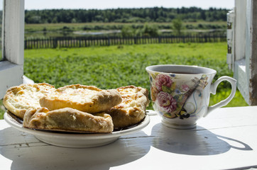 Delicious homemade pies and a cup of tea on the windowsill village background