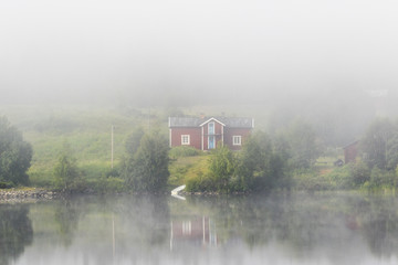 Red idyllic old cottage on a beach in fog