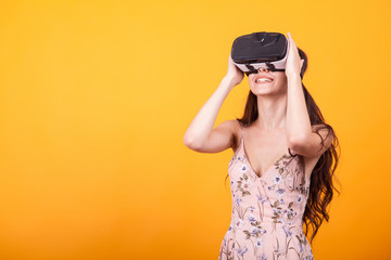 Young girl in virtual augmented reality helmet in studio over yellow background. Testing the application in virtual reality