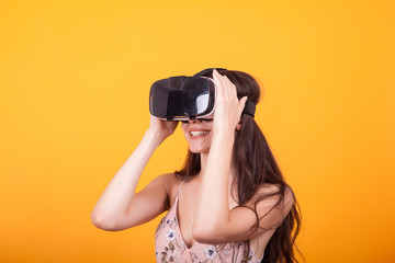 Smile happy woman getting experience using VR-headset glasses of virtual reality in studio over yellow background.
